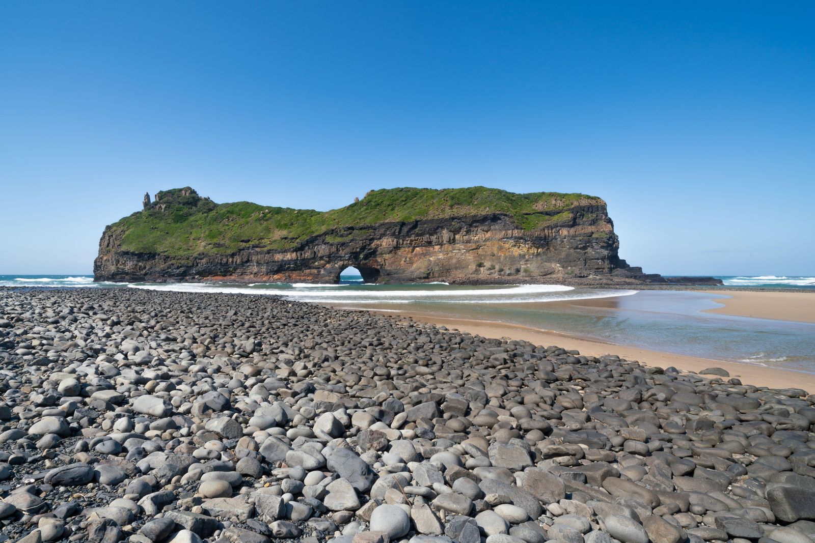 The Hole in the Wall, the rock arch off Coffee Bay on the Wild Coast, seen across a pebble beach